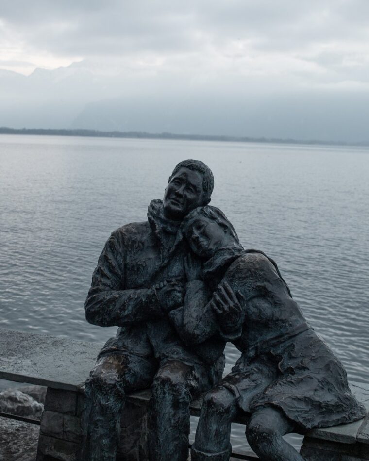 Escultura de dos figuras abrazadas frente a un mar gris al anochecer