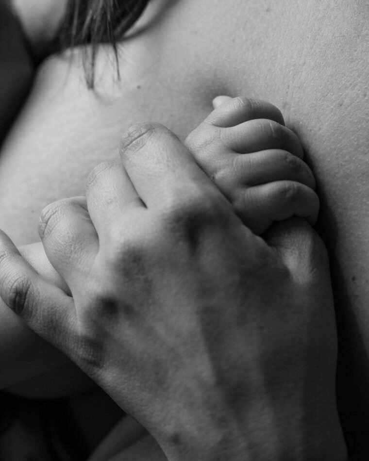 La mano de un bebé agarrada a la de su madre sobre su pecho, en blanco y negro