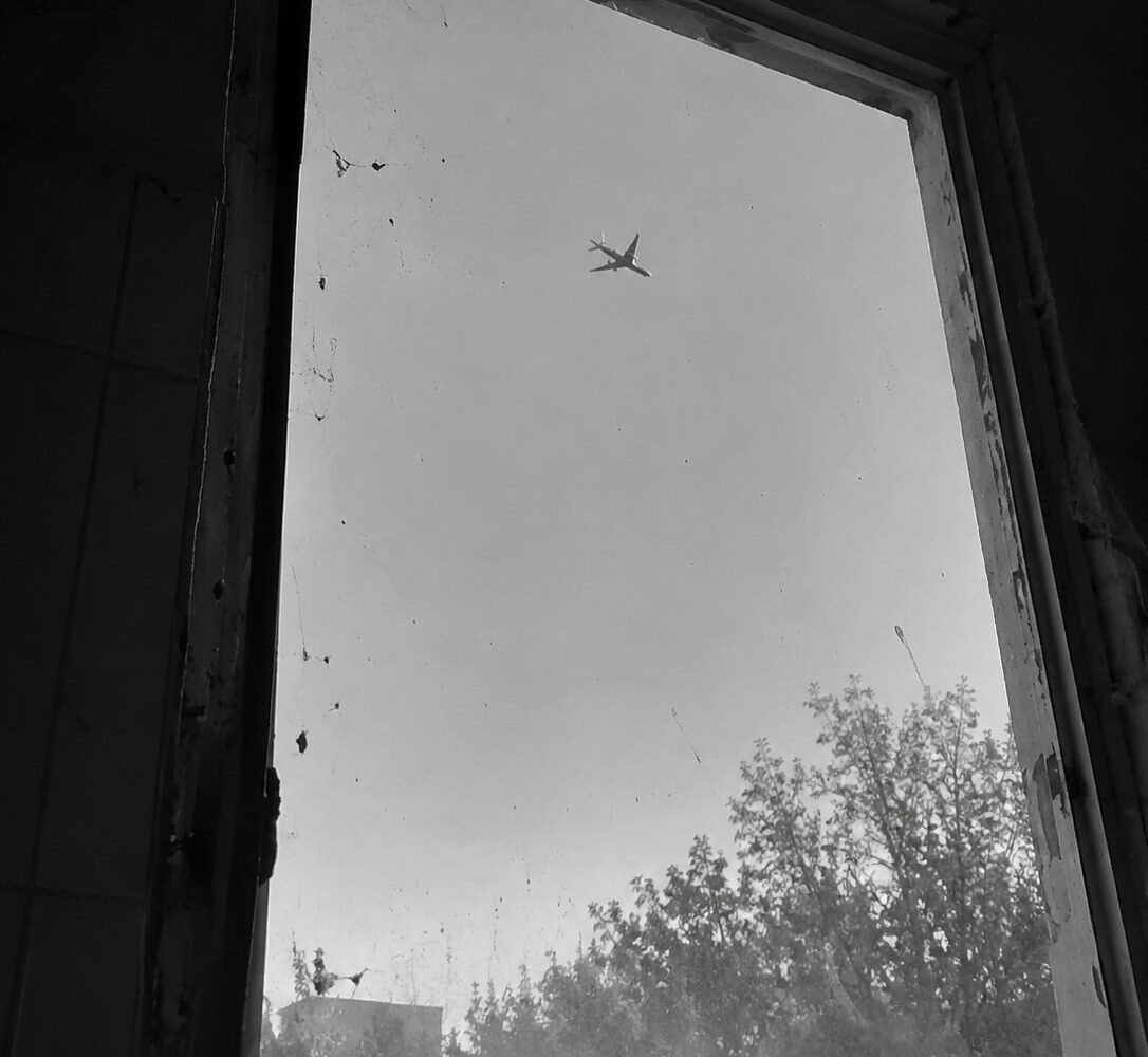 Un avión cruzando el cielo visto a través de una ventana sucia, en blanco y negro