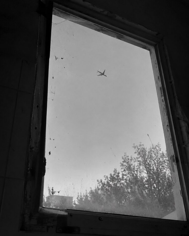 Un avión cruzando el cielo visto a través de una ventana sucia, en blanco y negro